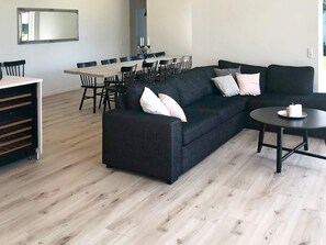 A modern living room with a sectional sofa, a dining table with chairs, and a small round table with candles. - 4 Star Holiday Home in Vaeggerlose (Vaeggerlose)