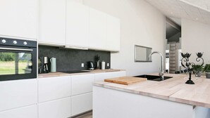 Une cuisine moderne avec des meubles blancs, un four encastré, une machine à café et un évier surmonté d’un miroir.
