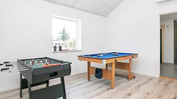 A room with a foosball table, a pool table, and a window with a view of trees.