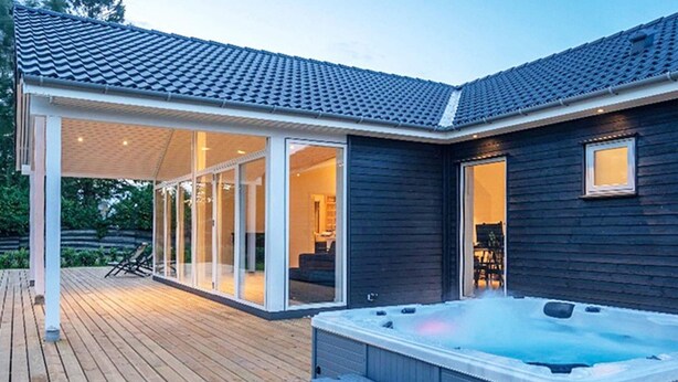 Un espace moderne aménagé à l’extérieur avec un bain à remous, une terrasse en bois, des portes coulissantes en verre donnant sur un espace de vie et un patio couvert.