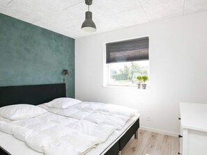 A bedroom with a bed, a window with blinds, a wall-mounted lamp, and a small potted plant on the windowsill. - 4 Star Holiday Home in Vaeggerlose (Vaeggerlose)