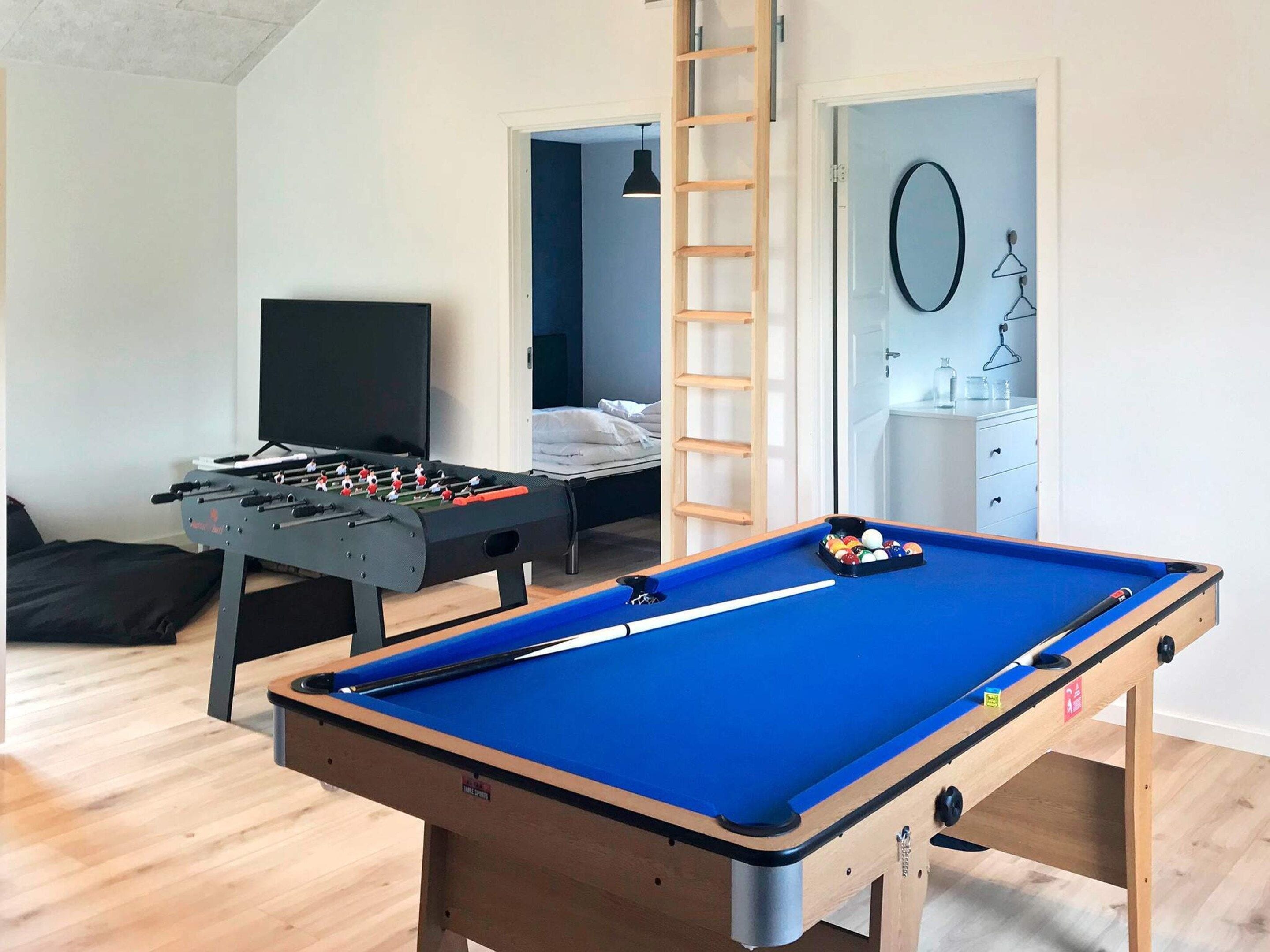 A room with a pool table, foosball table, and a bed with a ladder.