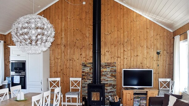 A cozy living room with a fireplace, wooden walls, a dining area with white chairs, and a flat-screen TV. - Holiday Home in Bjorli (Lesja)