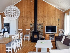 A cozy living room with a fireplace, wooden walls, a dining area with white chairs, and a flat-screen TV. - Holiday Home in Bjorli (Lesja)