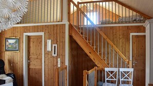 A wooden interior with a staircase leading to a loft bedroom. There is a dining area with a table and chairs, and a door with a picture frame. - Holiday Home in Bjorli (Lesja)