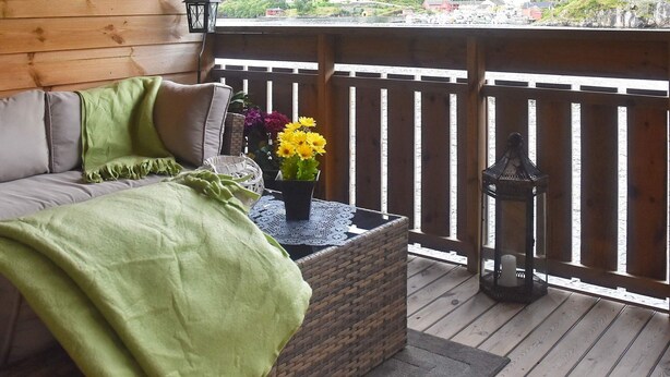 A wooden deck with a sofa, a wicker planter with flowers, and a lantern. - 4 Star Holiday Home in Leirvik i Sogn (Hyllestad)