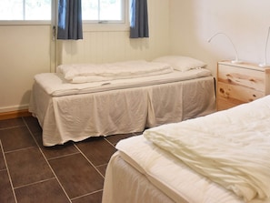 Une chambre à coucher avec un lit, une table de chevet, une commode et une fenêtre avec des rideaux.