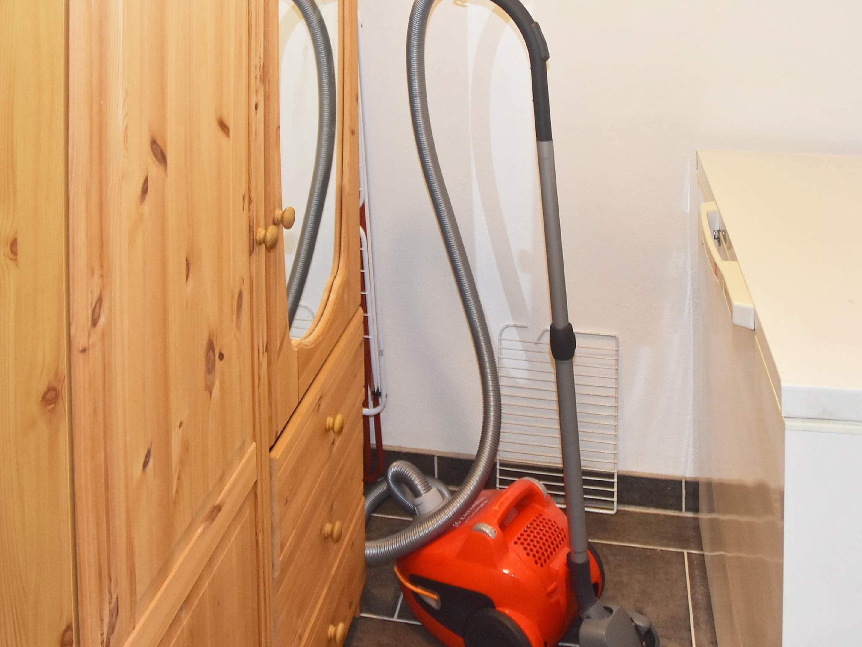 A wooden cabinet with a vacuum cleaner in a room with tiled flooring and a white wall.