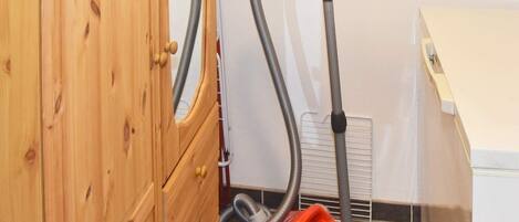 A wooden cabinet with a vacuum cleaner in a room with tiled flooring and a white wall.