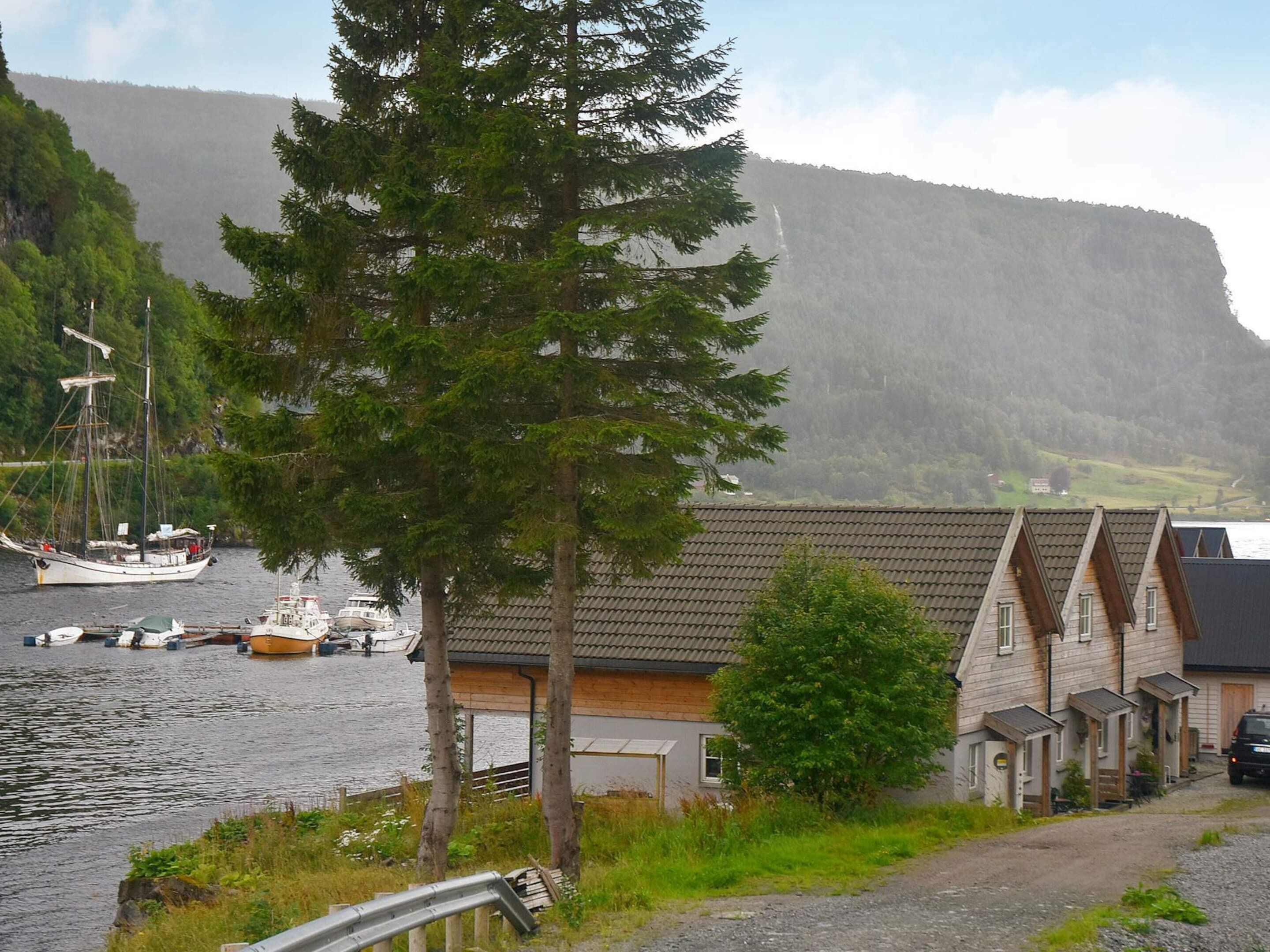 A coastal village with traditional wooden houses, a dock with boats, and a forested hillside in the background.