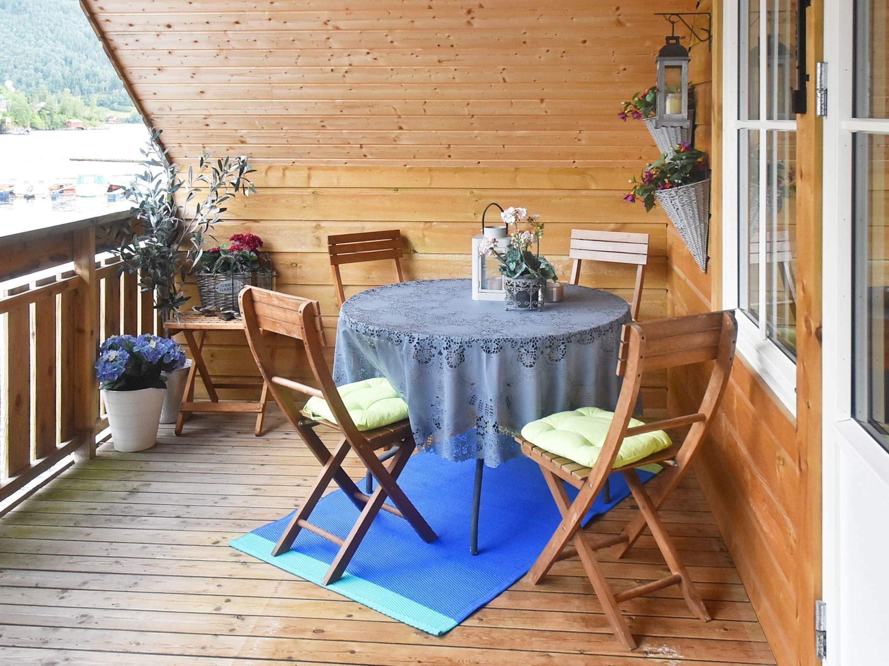 Une terrasse en bois avec une table ronde et des chaises, des plantes en pot et une lanterne.