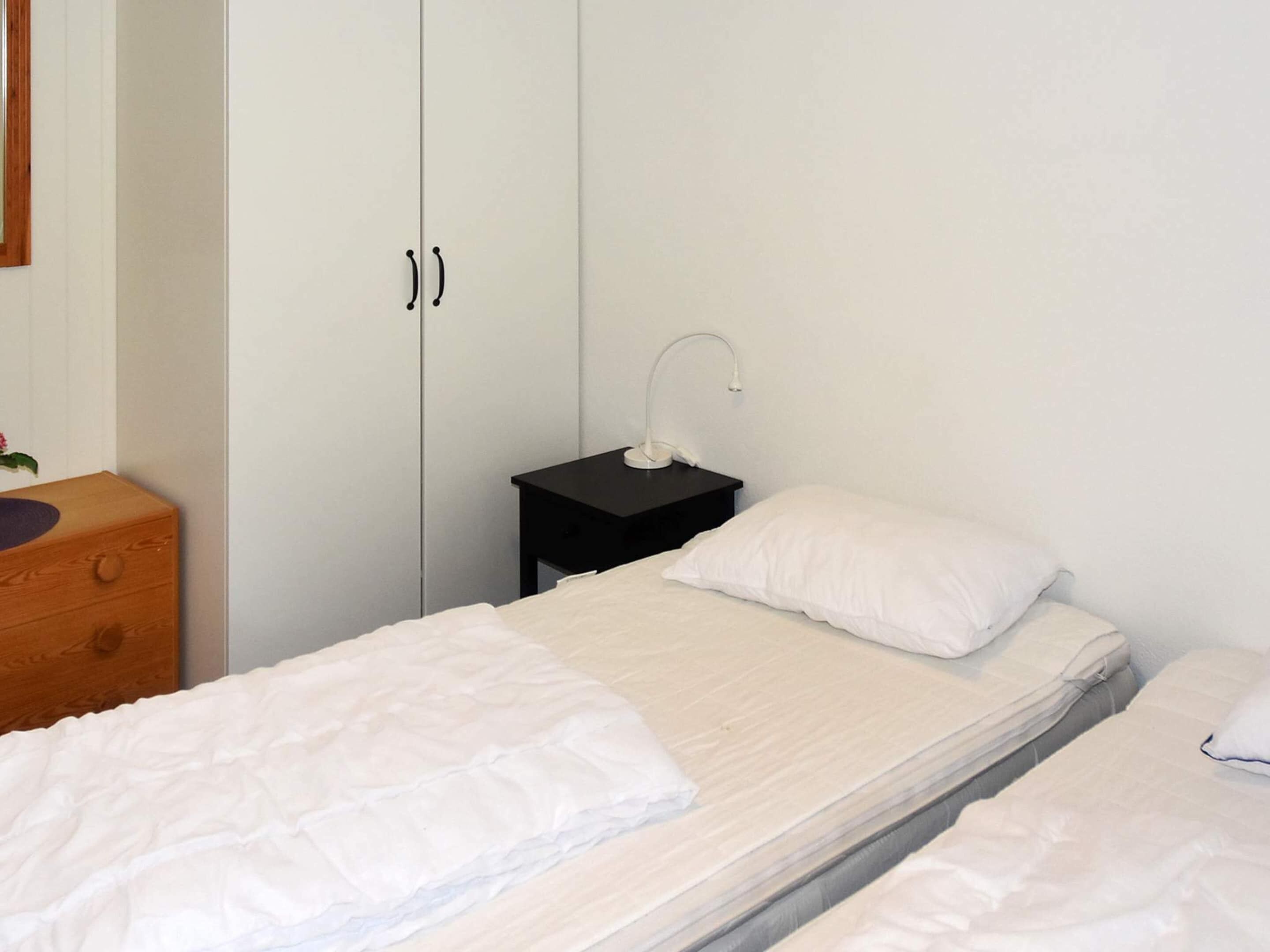 A bedroom with two single beds, a wooden dresser, a black nightstand with a lamp, and a white wardrobe.