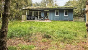 A small, single-story cabin with a covered porch, a dining table, and a grill outside.
