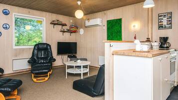 Un espacio habitable compacto con un sillón de cuero negro, una mesita redonda pequeña, un televisor y una zona de kitchenette.