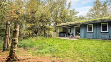 Eine Hütte mit überdachter Terrasse, Grill und Blick auf den umliegenden Wald.
