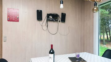 Ein Zimmer mit einem Tisch, einer Weinflasche, einem Notizbuch, einer Lampe und Lautsprechern an der Wand.