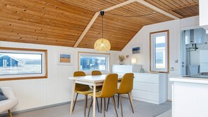 A modern kitchen with white cabinetry, a dining area with a white table and mustard chairs, wooden ceiling beams, and large windows. - 4 Person Holiday Home in Lemvig (Lemvig)