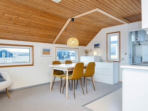 A modern kitchen with white cabinetry, a dining area with a white table and mustard chairs, wooden ceiling beams, and large windows.