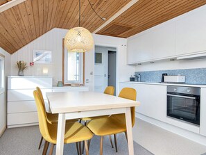 A modern kitchen with a wooden ceiling, a dining table with chairs, and a built-in oven. - 4 Person Holiday Home in Lemvig (Lemvig)