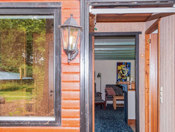 A wooden exterior with a glass door leading to an interior with a blue patterned carpet, a painting, and a chair.