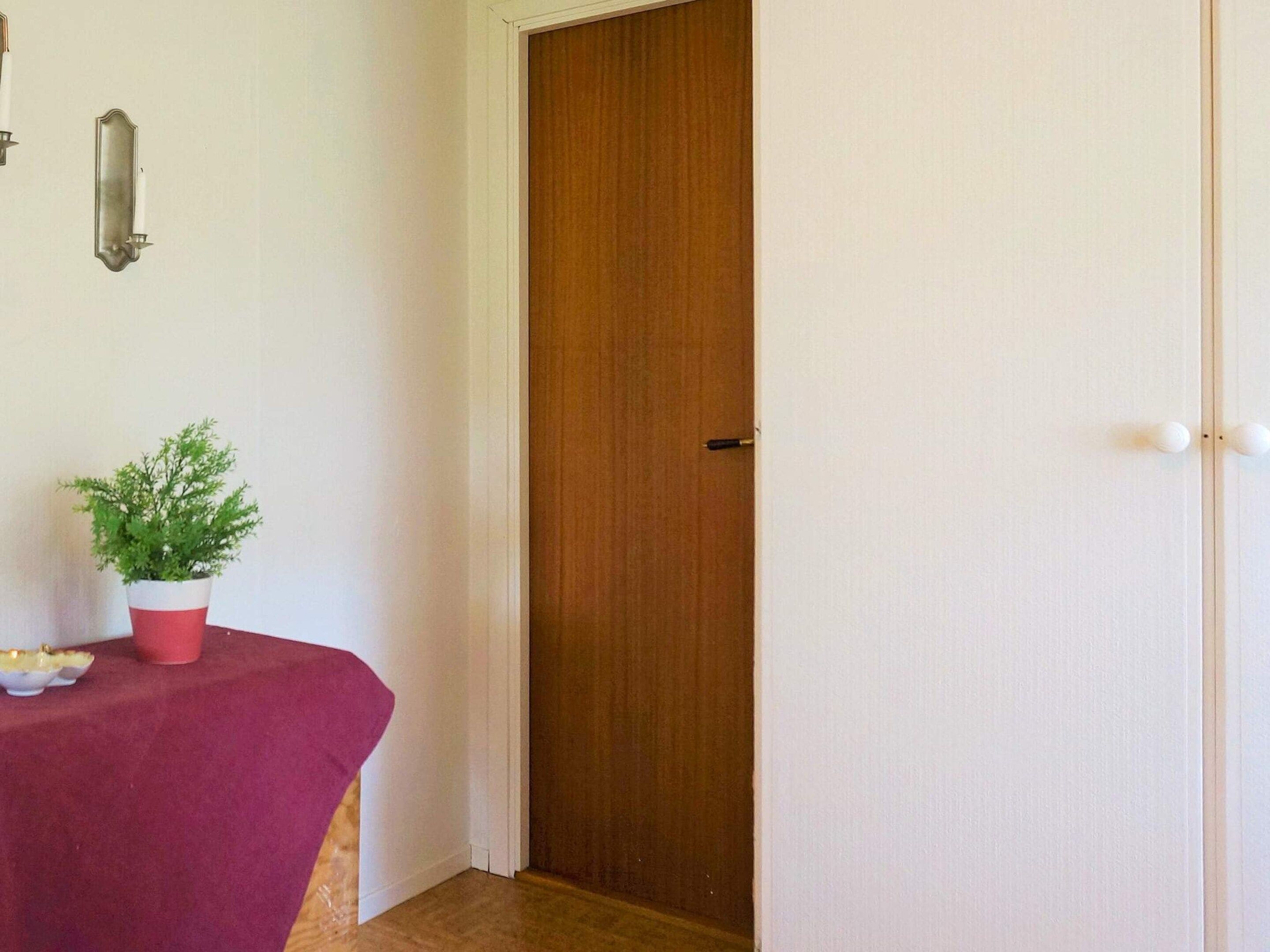A room with a wooden door, a small table with a plant, and a red tablecloth.