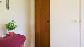 A room with a wooden door, a small table with a plant, and a red tablecloth.