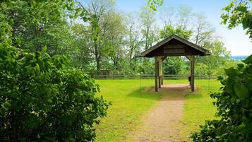 A wooden gazebo with a sign reading 'HUSABY INFOPLATS' in a grassy area surrounded by trees.