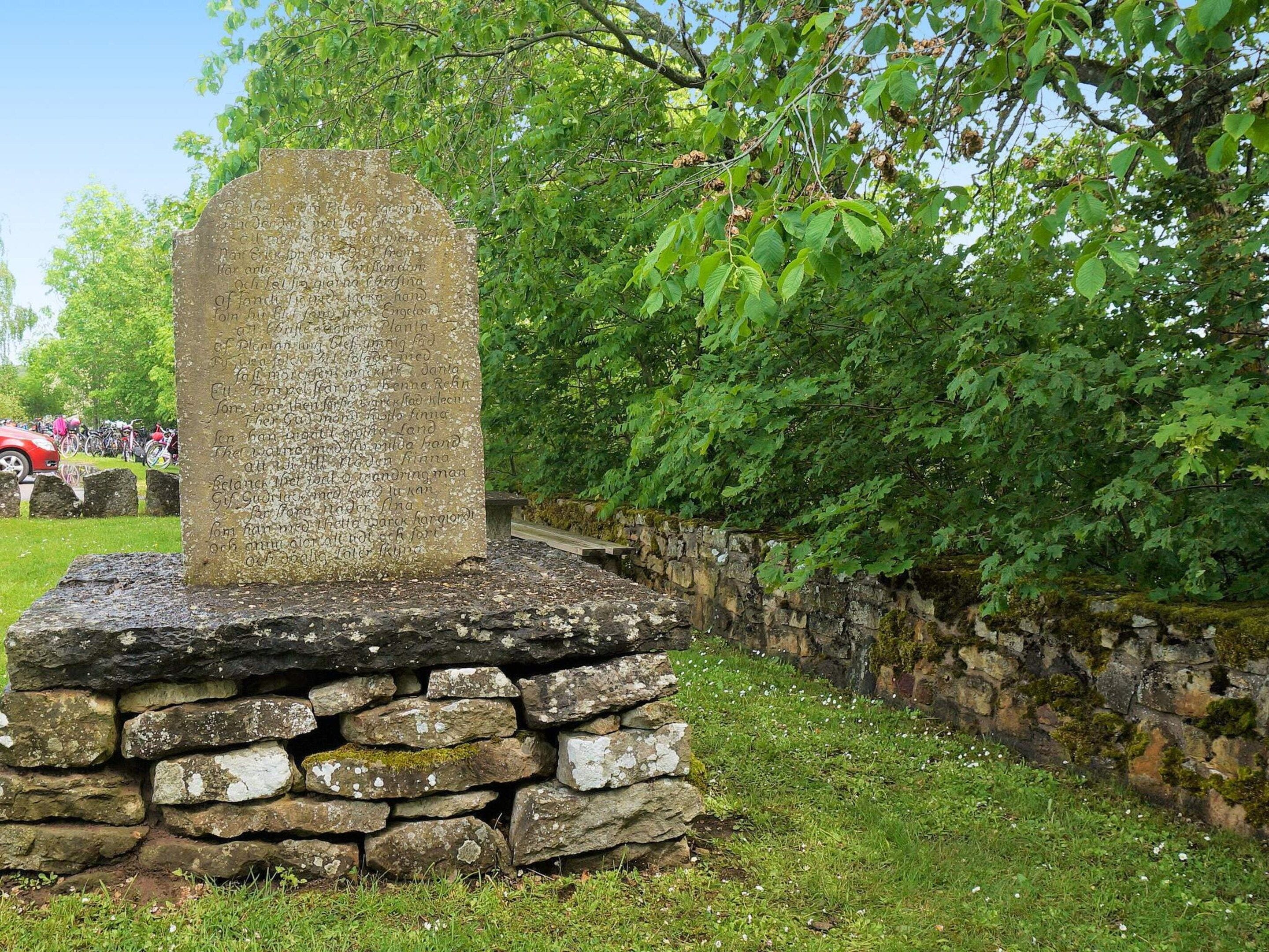 A stone monument with inscriptions, surrounded by a stone wall and greenery.