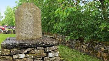 A stone monument with inscriptions, surrounded by a stone wall and greenery.