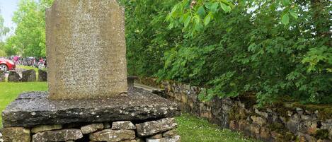 A stone monument with inscriptions, surrounded by a stone wall and greenery.