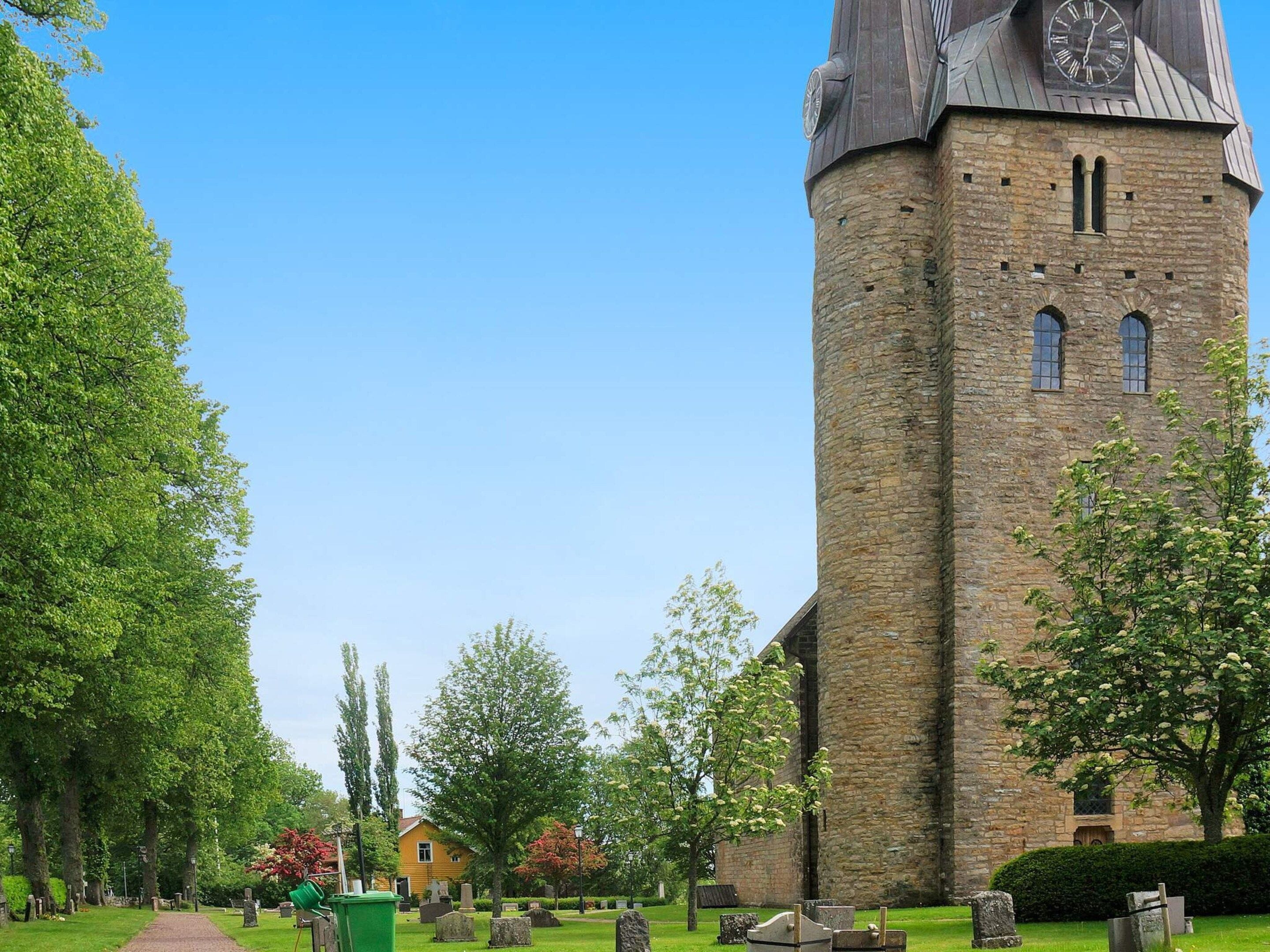 A church with a tall tower and a clock, surrounded by a cemetery with headstones and trees.