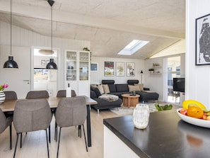 Un salon moderne comprenant un canapé, une table à manger et des chaises, un coin cuisine avec des placards et une lucarne.