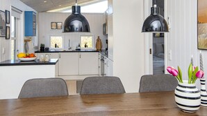 A modern kitchen with pendant lights, a dining area with a wooden table, and a view of the outdoors. - Mod Holiday Home in Jutland near Sea (Lemvig)