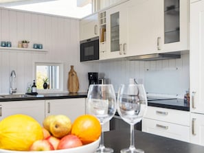 Une cuisine moderne avec des meubles blancs, un plan de travail noir et un saladier rempli de fruits.
