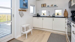 A modern kitchen with white cabinets, a blue accent wall, and a small white stool. - Mod Holiday Home in Jutland near Sea (Lemvig)