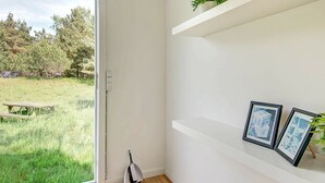 A room with a large window, a broom, and two framed pictures on a white shelf. - Serene Holiday Home in Bornholm With Terrace (Akirkeby)