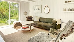 A modern living room with a green sofa, a round coffee table, a white armchair, and a large window offering a view of greenery. - Serene Holiday Home in Bornholm With Terrace (Akirkeby)