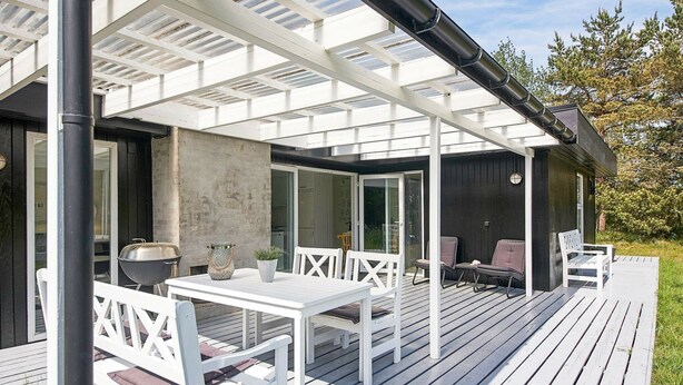 A covered outdoor patio with a table and chairs, a grill, and a potted plant. - Serene Holiday Home in Bornholm With Terrace (Akirkeby)
