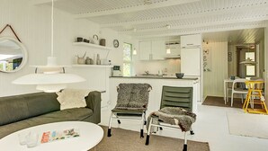 A modern, minimalist living room with a sofa, chairs, a coffee table, and a kitchen area in the background. - Serene Holiday Home in Bornholm With Terrace (Akirkeby)