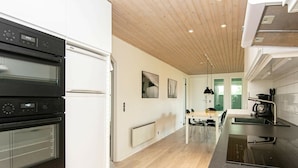 A modern kitchen with two ovens, a dining area with a table and chairs, and a view of the outdoors through a glass door. - Elegant Holiday Home in Jutland With Sauna (Horsens)