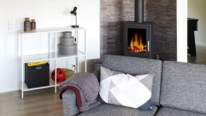Una sala de estar moderna con un sofá gris, una estantería blanca y una chimenea de leña.
