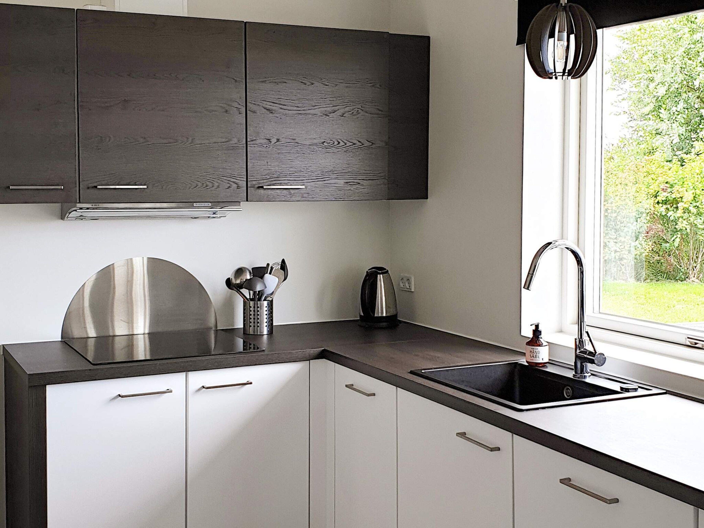Une cuisine moderne avec des meubles en bois foncé, des appareils électroménagers en acier inoxydable et une fenêtre donnant sur un paysage verdoyant.