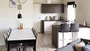 Una cocina moderna con armarios oscuros, una isla central con taburetes altos y una zona de comedor con mesa y sillas blancas.