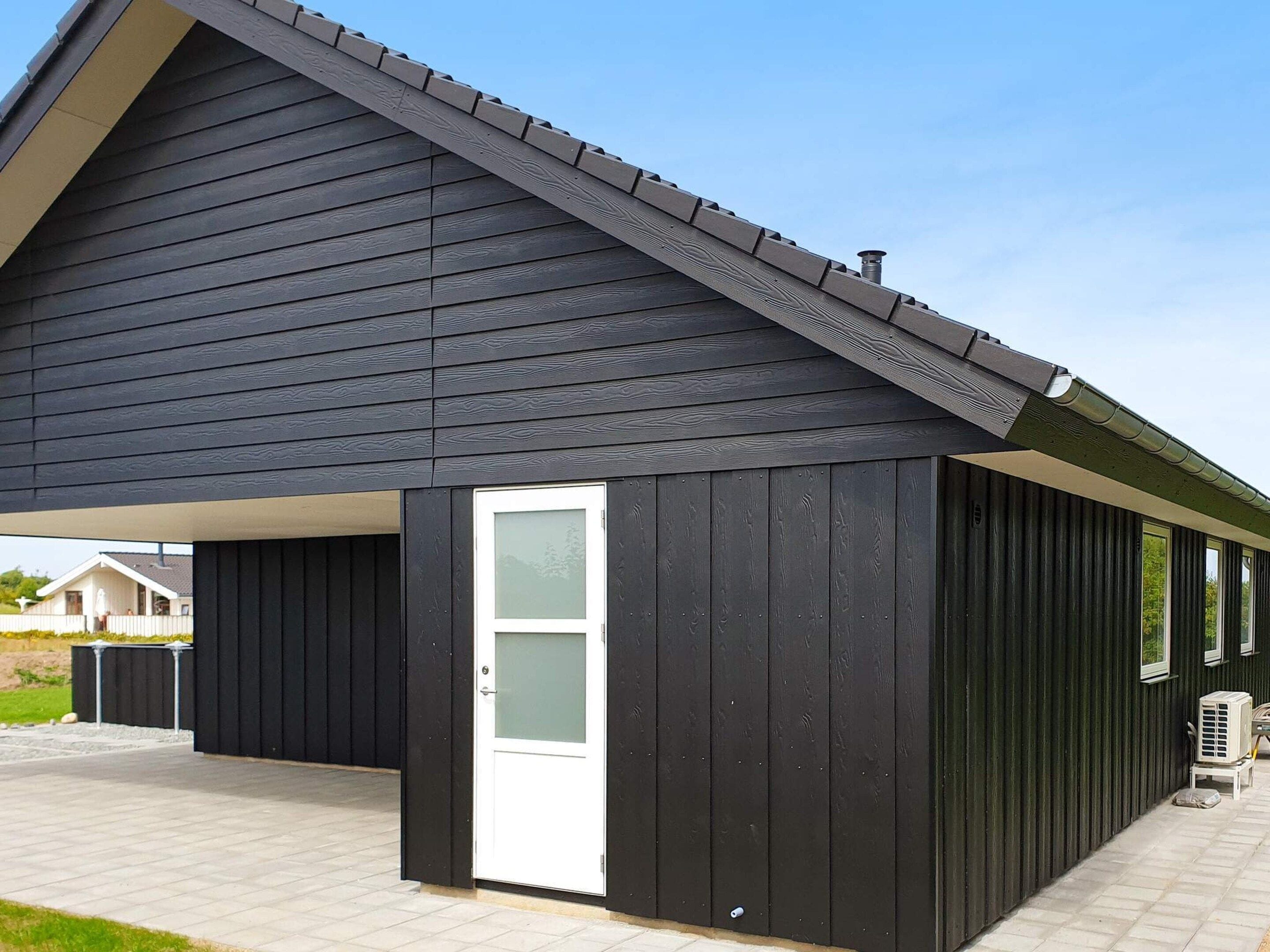 Een gebouw met een donkere gevel, een witte deur en een overdekt terras.