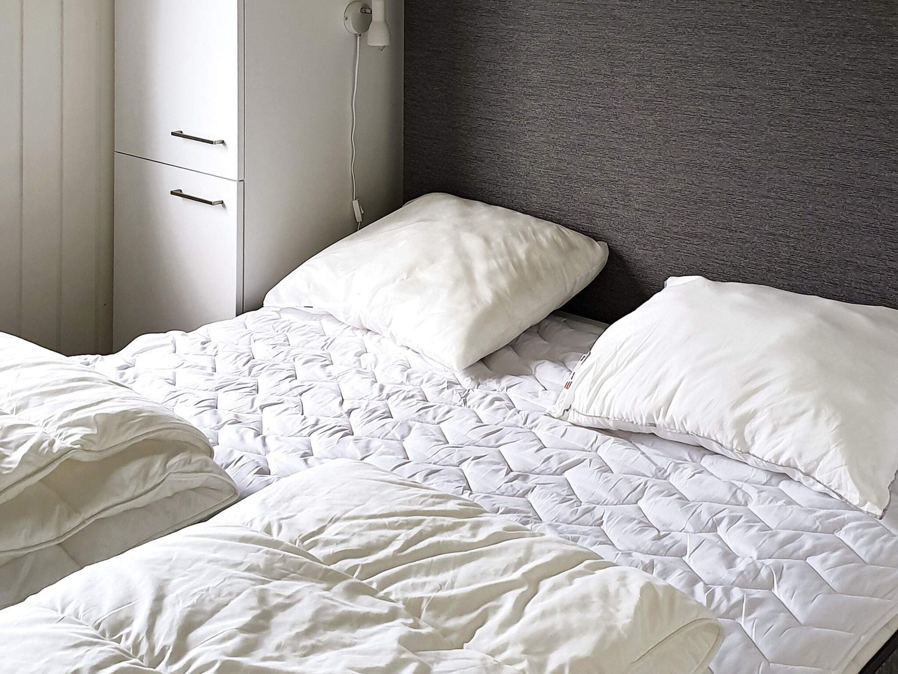Una cama con edredón blanco acolchado, dos almohadas y cabecera gris.