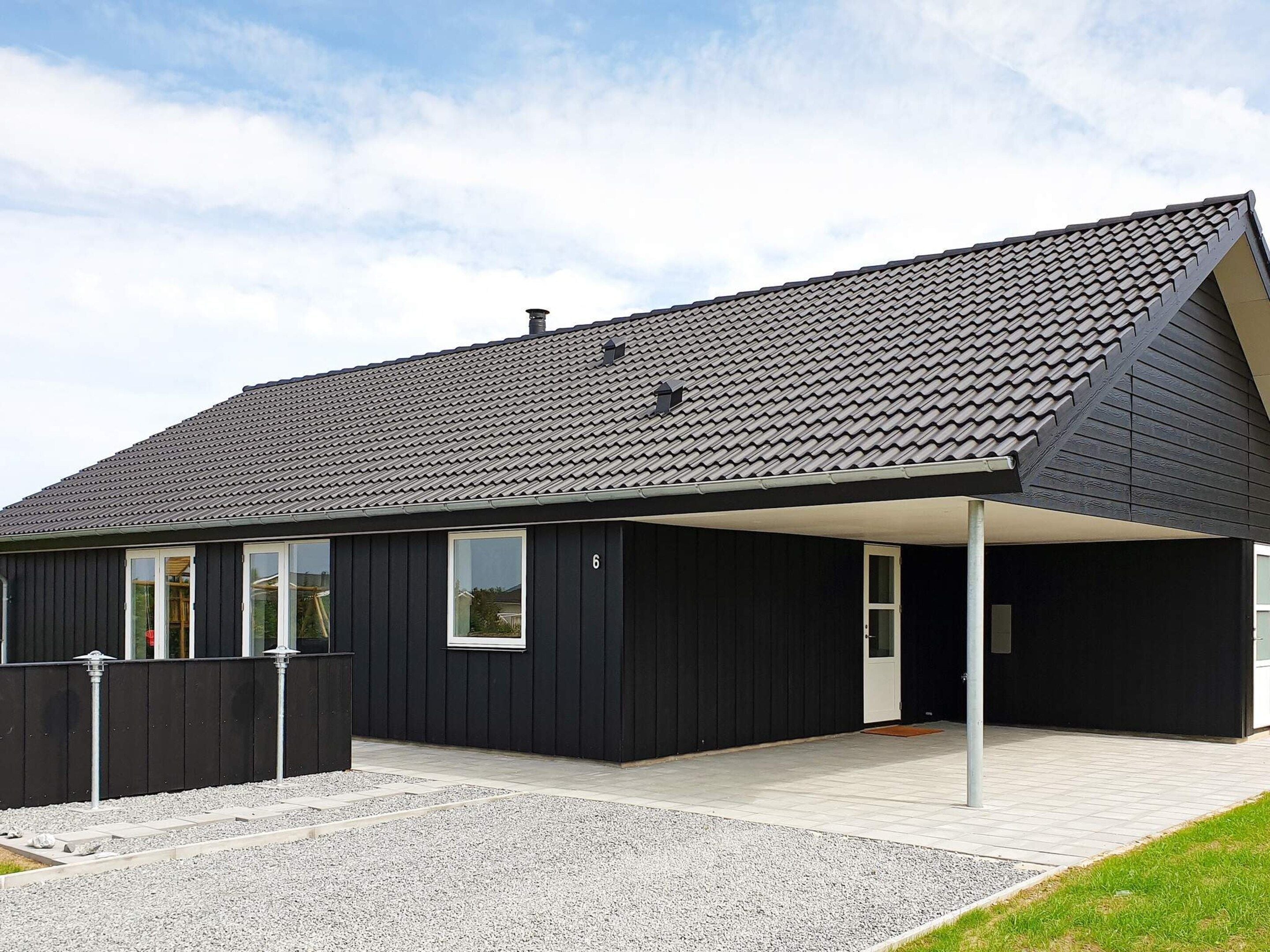 Un bâtiment moderne à la façade sombre, doté d’un toit en pente et d’un espace extérieur abrité.