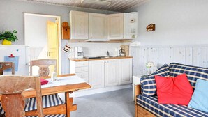 A compact kitchen with white cabinets, a wooden table, and a sofa with plaid cushions. - 4 Person Holiday Home in Arjang (Årjäng)