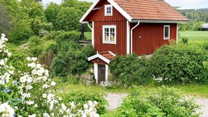 A red wooden house with a sloped roof, surrounded by lush greenery and white flowers. - 4 Person Holiday Home in Arjang (Årjäng)