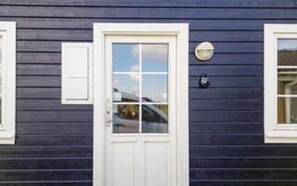 Et hus med en hvid hoveddør, et lille vindue med hvid ramme og en udendørs lampe.