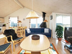 A modern living room with a wooden ceiling, a blue sofa, a wooden dining table, and a television.